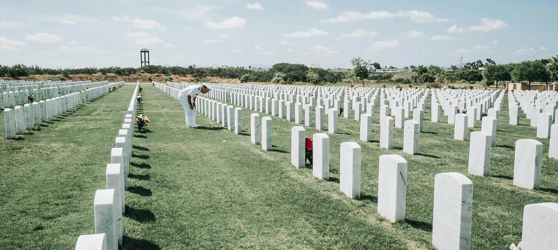 A man in white shirt standing next to a field of white tombstones.